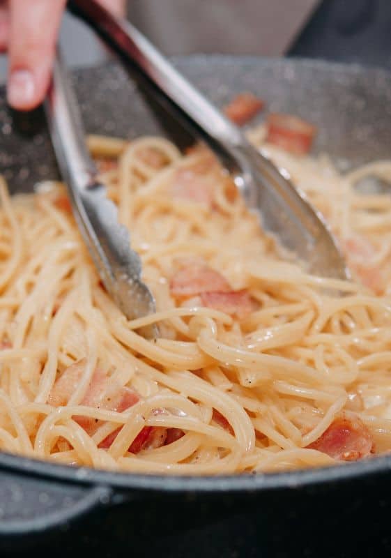 Tossing Cooked Pasta in the Sauce: Cooked spaghetti being tossed in the creamy sauce, evenly coated.