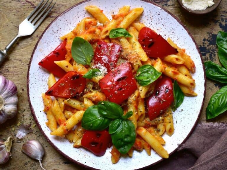 Vegetarian Rasta Pasta - A vibrant dish of penne pasta coated in a creamy tomato sauce with colorful red bell peppers and aromatic jerk seasoning, creating a burst of flavors on the plate.