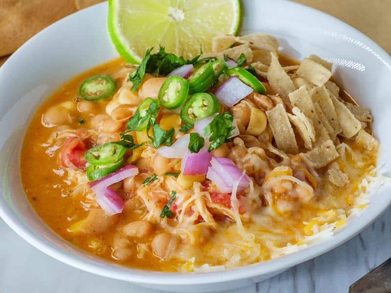 A close-up of a comforting bowl of White Bean Chicken Chili, garnished with jalapeno slices and a squeeze of lime.