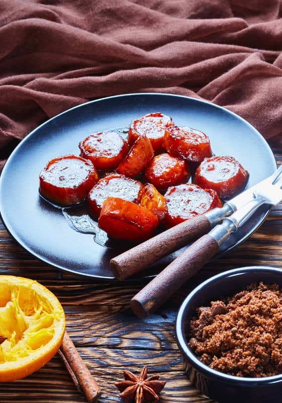 Candied sweet potatoes served in a blue plate, glistening with a caramelized sugar glaze and lightly seasoned with cinnamon and nutmeg.