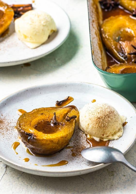 Baked pears in caramel sauce and spices server on a white plate with a side of vanilla ice cream.