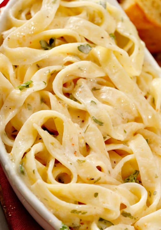 A close-up image of creamy roasted garlic pasta, topped with freshly grated parmesan cheese and a sprinkle of black pepper, served on a rustic white plate. The pasta is coated in a rich, buttery sauce, and the strands of fettuccine shine with a mouthwatering gloss, inviting you to dig in for a quick and satisfying weeknight dinner.