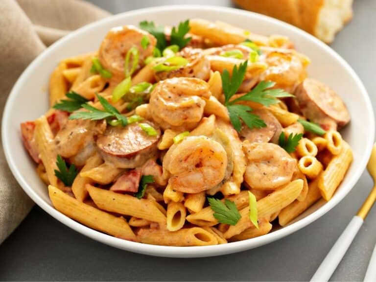 A hearty plate of Cajun Shrimp and Sausage Pasta, topped with fresh parsley and served with a side of garlic bread. The pasta is coated in a creamy, spicy Cajun sauce with pieces of tender shrimp and flavorful slices of andouille sausage visible throughout the dish.