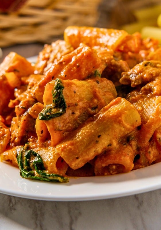 Close-up view of Italian sausage rigatoni and fresh basil served on a white plate.