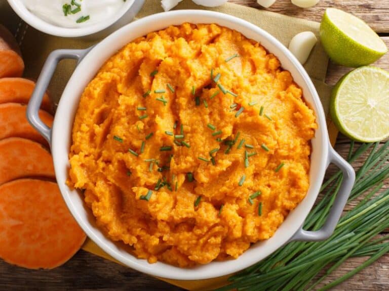 A close-up top image view of creamy mashed sweet potatoes garnished with fresh chives in a serving dish, displaying its velvety texture and vibrant orange color.