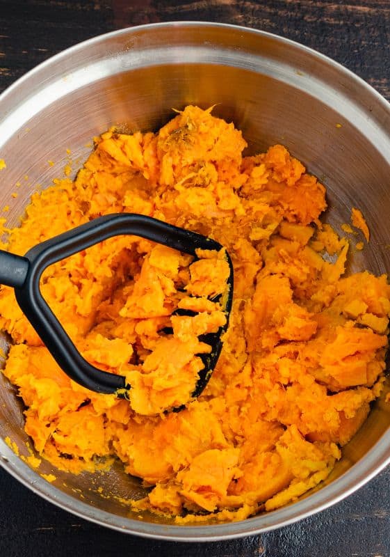 Mashing sweet potatoes with a masher in a bowl.