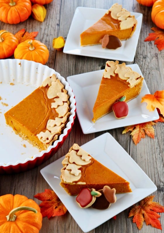 Pumpkin pie slicees on white plate and small pumpkin decorating the table.