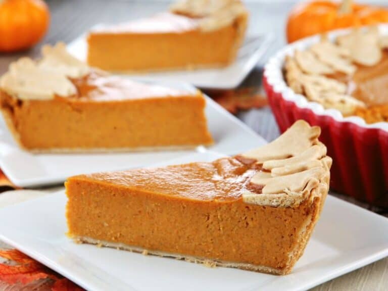 Pumpkin pie slices on white plate and small pumpkin decorating the table.
