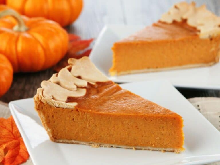 Pumpkin pie slices on white plate and small pumpkin decorating the table.