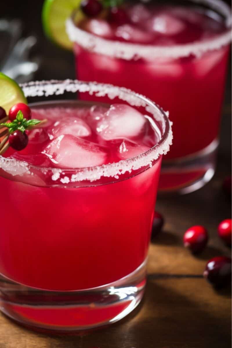 A vibrant red Cranberry Margarita garnished with a lime wheel and fresh cranberries, served in a salt-rimmed glass.