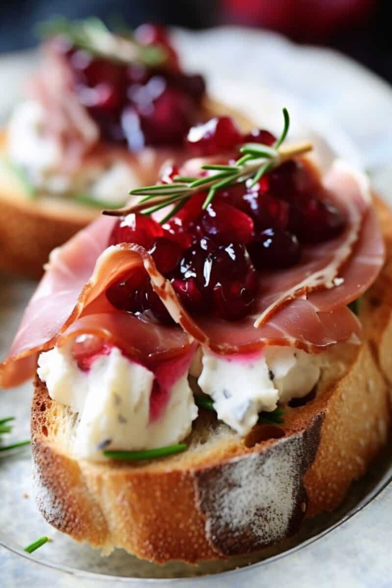 Close-up of a single Cranberry and Prosciutto Crostini, showcasing the vibrant red cranberry sauce and delicate prosciutto folds.