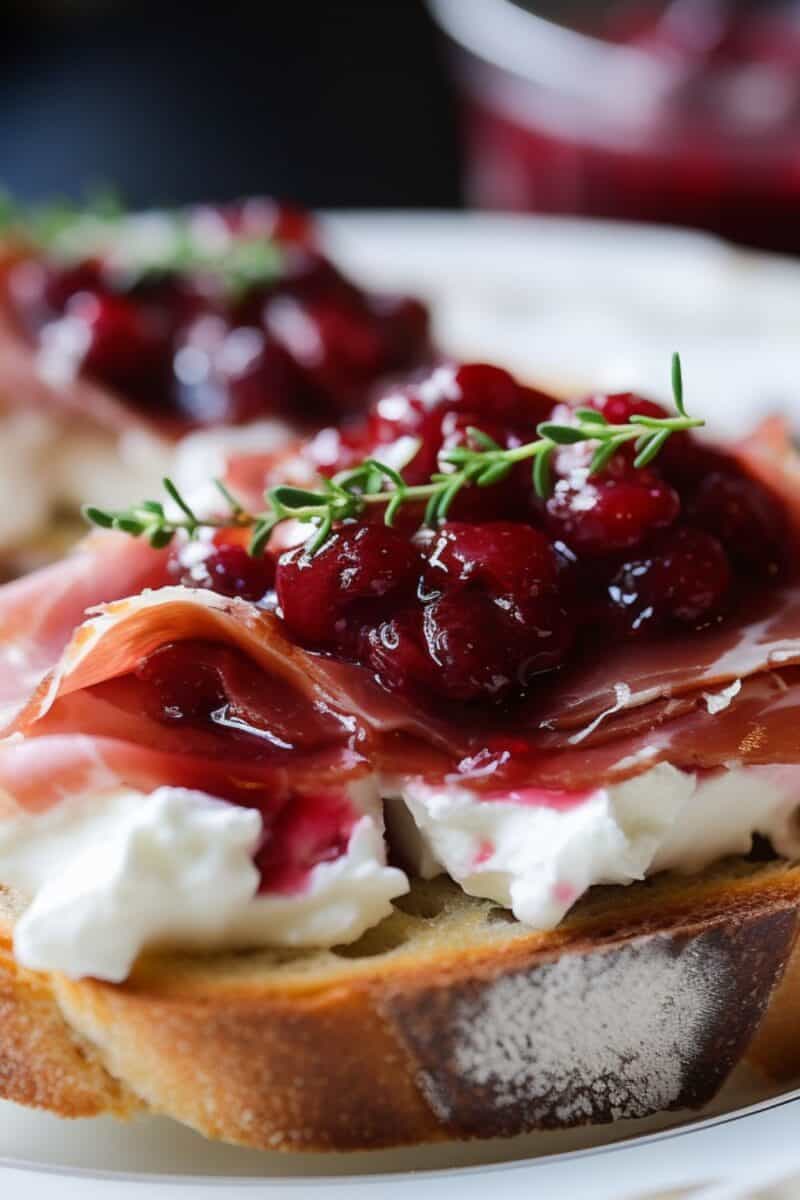 Close-up of Cranberry and Prosciutto Crostini on a white plate, showcasing the vibrant cranberry topping.