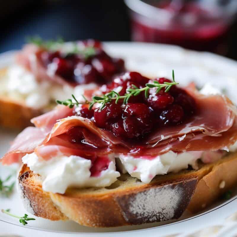 Close-up view of Cranberry and Prosciutto Crostini with a vibrant red cranberry sauce and thin prosciutto slice