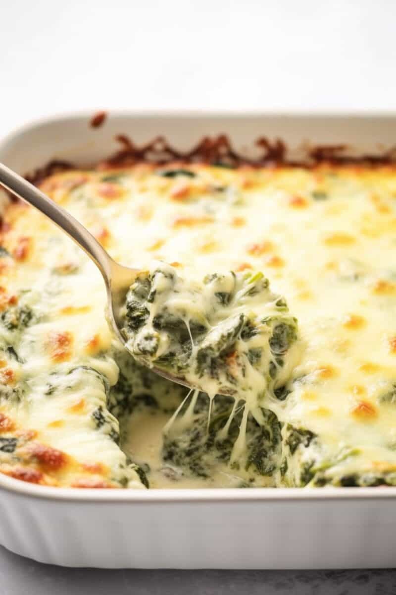 Close-up of a serving spoon scooping out a portion of Spinach Gratin, revealing layers of creamy spinach and melted cheese.