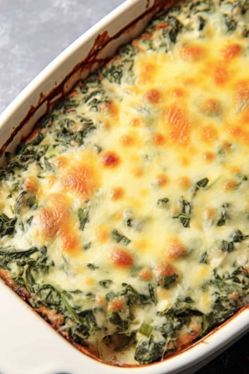 Top view of A golden-brown Spinach Gratin fresh out of the oven, showcasing a crispy cheese topping and creamy spinach filling in a ceramic baking dish.