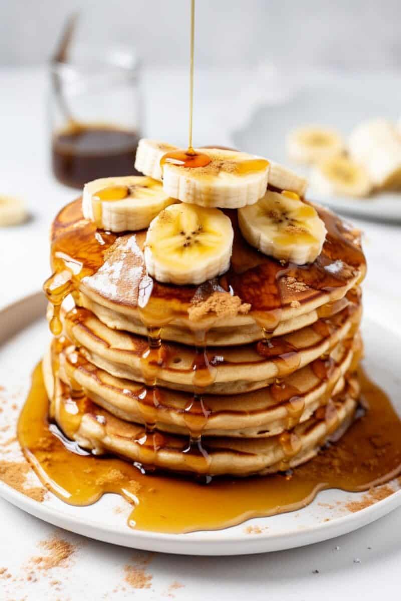 Homemade banana pancakes on a plate, topped with sliced bananas and maple syrup, showcasing a fluffy texture and golden-brown color.