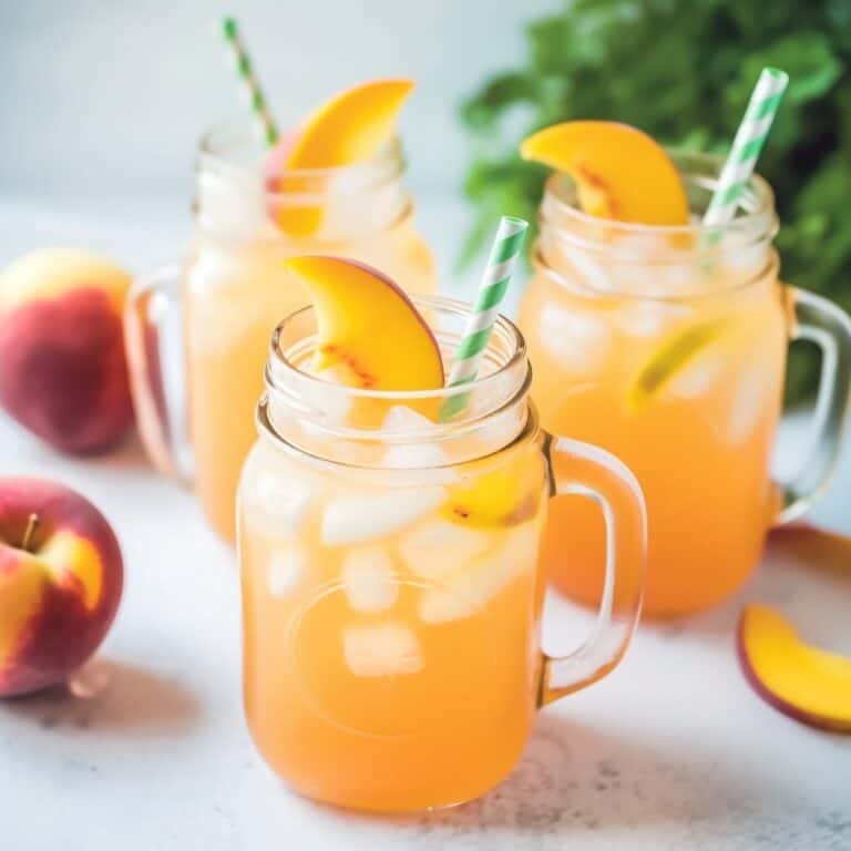 Three mason jars filled with vibrant peach lemonade, ice cubes floating at the top, and garnished with fresh peach slices and mint leaves, conveying a sense of homemade simplicity and summer joy.