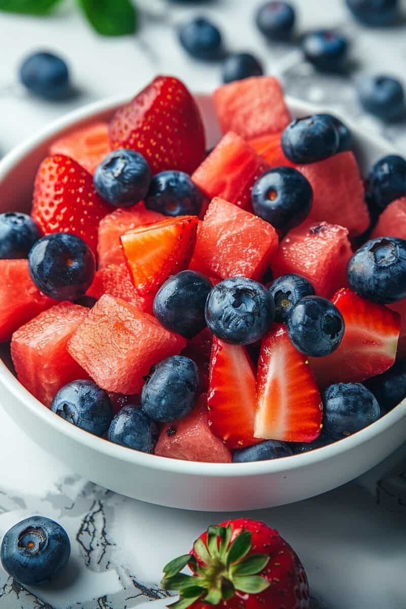 Bright bowl of watermelon, strawberries, and blueberries with mint, ready for summer.