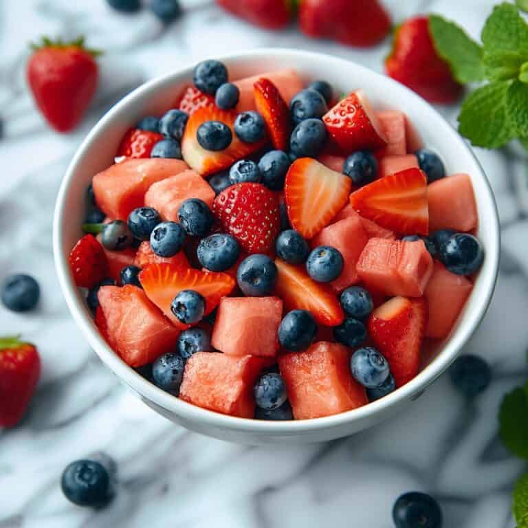 A colorful bowl of Berry Watermelon Fruit Salad, featuring chunks of juicy watermelon, ripe strawberries, and plump blueberries, garnished with fresh mint leaves and drizzled with a lime juice and powdered sugar dressing, showcasing a refreshing and healthy summer treat.