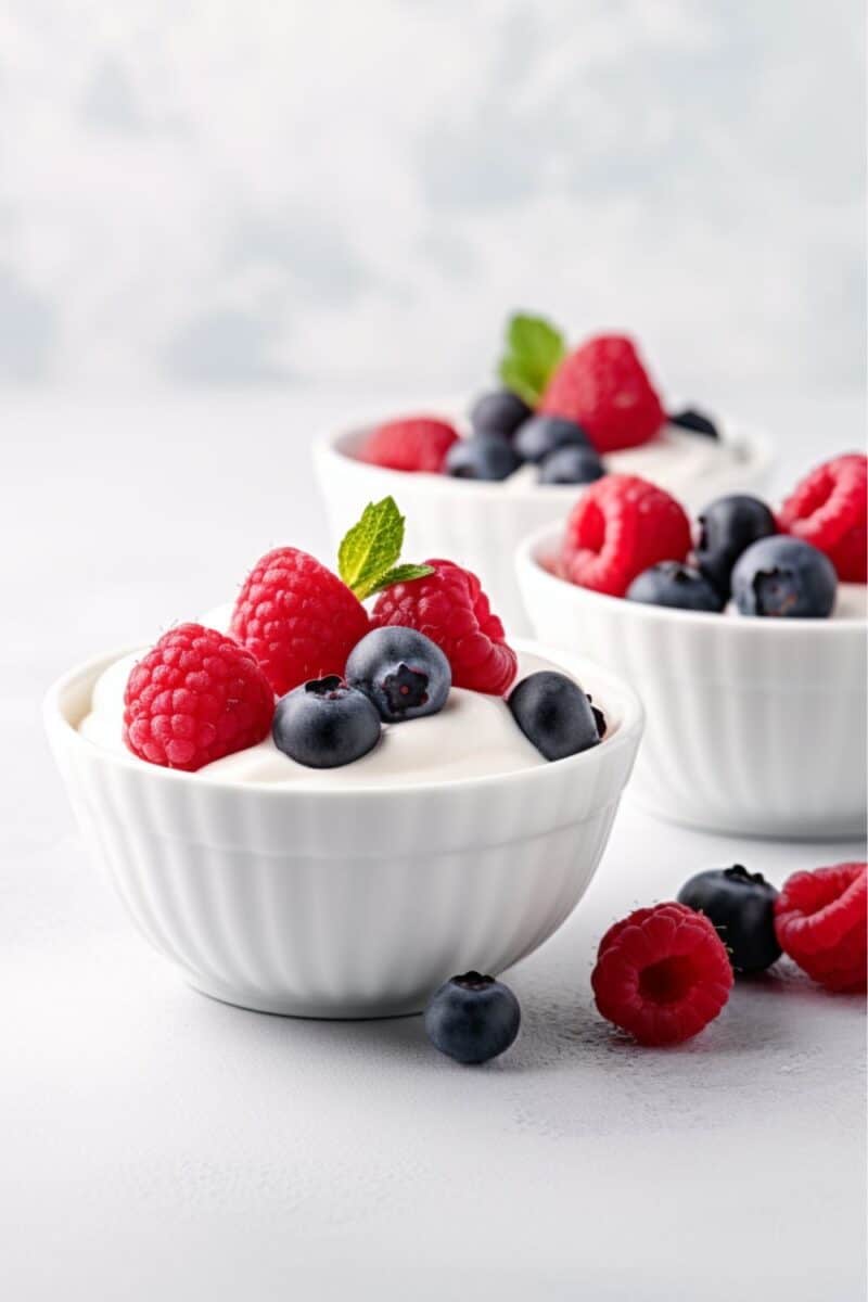 Three bowls of creamy Greek yogurt, each adorned with fresh blueberries, raspberries, present a colorful and nutritious option for a quick breakfast, snack, or healthy dessert.