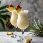 A frosty glass of Piña Colada garnished with a pineapple slice and cherry, showcasing the creamy coconut and pineapple juice blend with a hint of rum, ready to be enjoyed at a summer beach party.