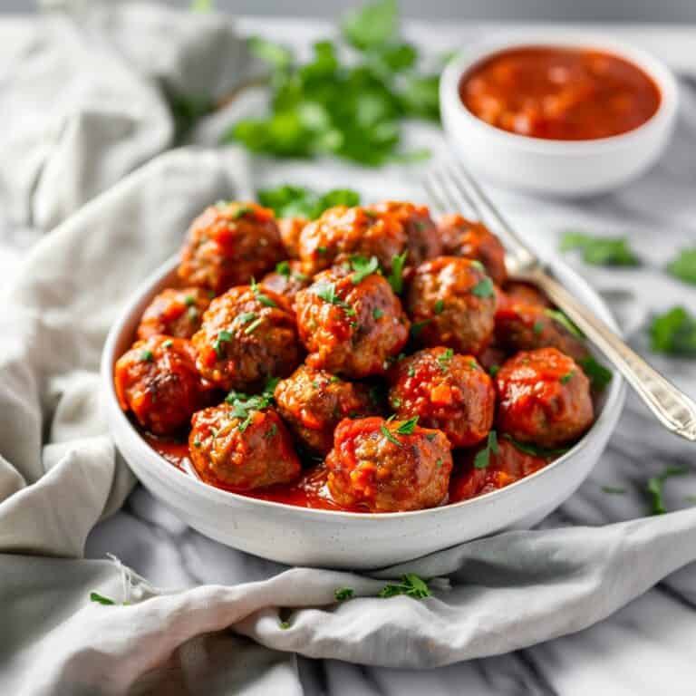 A warm, inviting bowl of Italian Meatballs nestled in a rich, homemade tomato sauce, garnished with fresh basil.