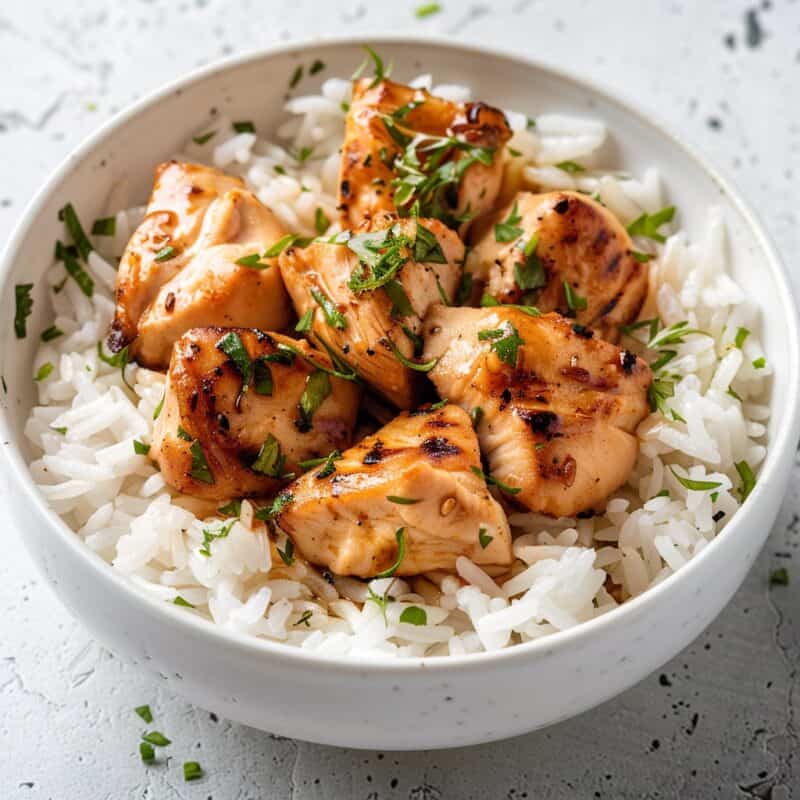 A bowl of Chili Lime Chicken with Fluffy White Rice, showcasing tender grilled chicken pieces seasoned with a spicy and tangy chili lime glaze atop a bed of steamed white rice. The chicken is garnished with fresh cilantro and lime wedges, adding vibrant color and freshness to the dish.