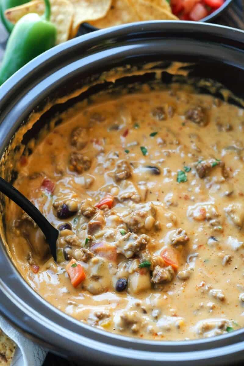 Overhead image of a Crock Pot filled with rich, creamy Queso with Beef and Sausage, featuring a spoon resting inside the pot, ready to serve.