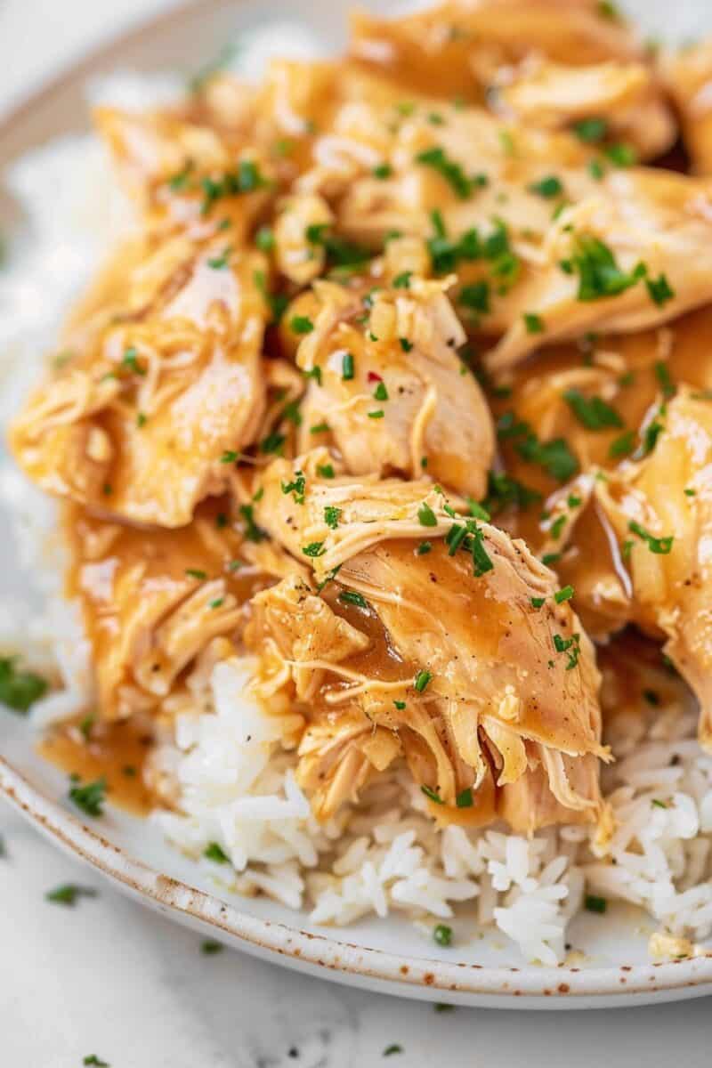 Crockpot chicken and gravy poured over fluffy white rice on a plate, ready to eat.