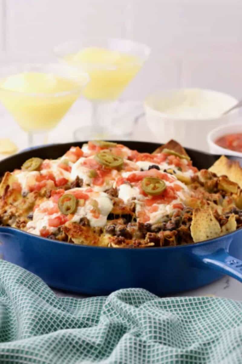 A vibrant and tempting skillet of Macho Nachos, layered with seasoned ground beef, melted cheese, and colorful toppings like jalapenos, olives, and tomatoes.