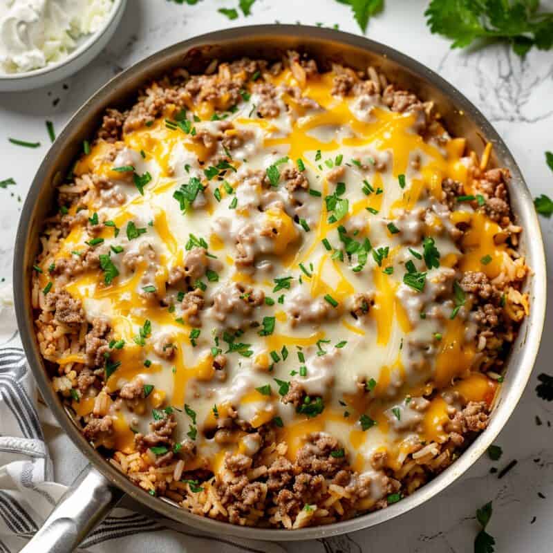 A Ground Pork and Rice Skillet Dinner presented in a sleek white stainless steel pan, showcasing a delicious meld of seasoned ground pork and fluffy rice, accented with a touch of green herbs, creating a harmonious and appetizing meal ready to be served.