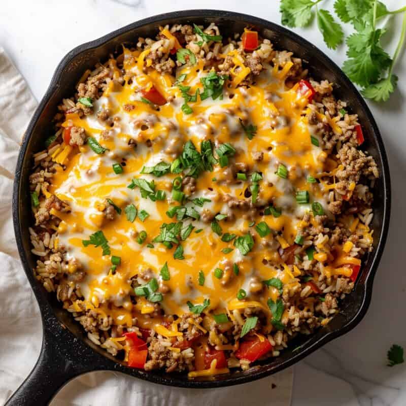 A savory Ground Turkey and Rice Skillet meal served in a cast iron skillet, featuring perfectly cooked, fluffy rice mixed with seasoned ground turkey, all generously topped with melted cheese that stretches invitingly with each scoop.