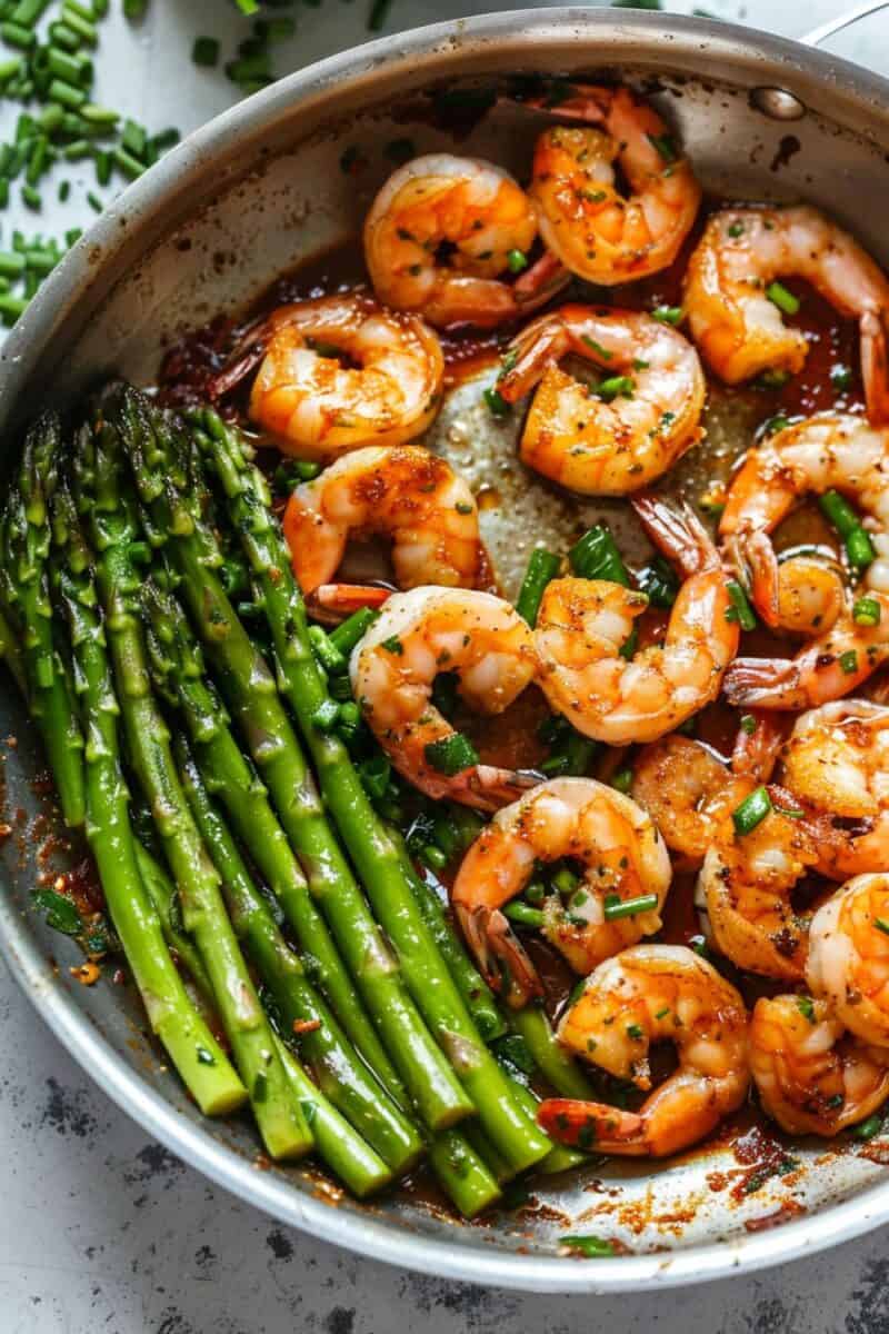 Close-up of lemon-glazed shrimp and asparagus in a skillet, hinting at a quick and delicious dinner option.