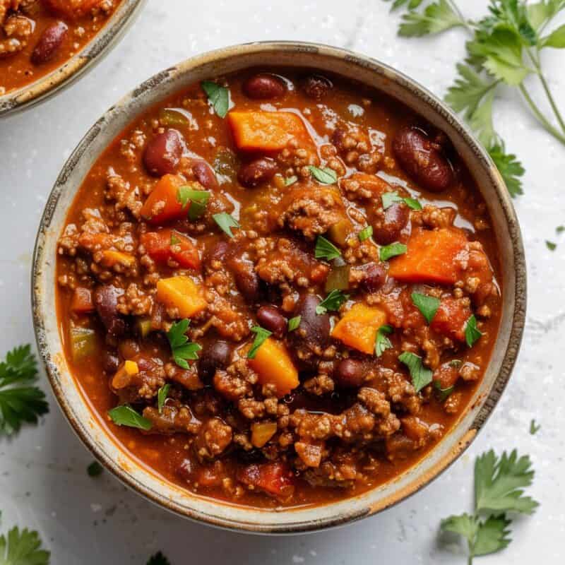 A bowl of hearty chili, brimming with seasoned ground beef, beans, and tomatoes, garnished with shredded cheese and a dollop of sour cream, ready to be enjoyed. The perfect ground beef recipe.