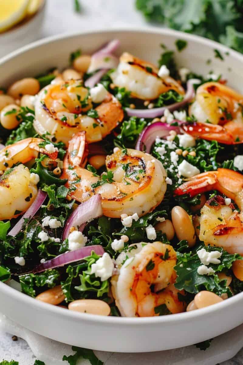 Close-up of a hearty Kale and White Bean Salad, An Erewhon Copycat Recipe featuring succulent shrimp, onion slices, and a sprinkle of feta cheese, dressed in a zesty vinaigrette.