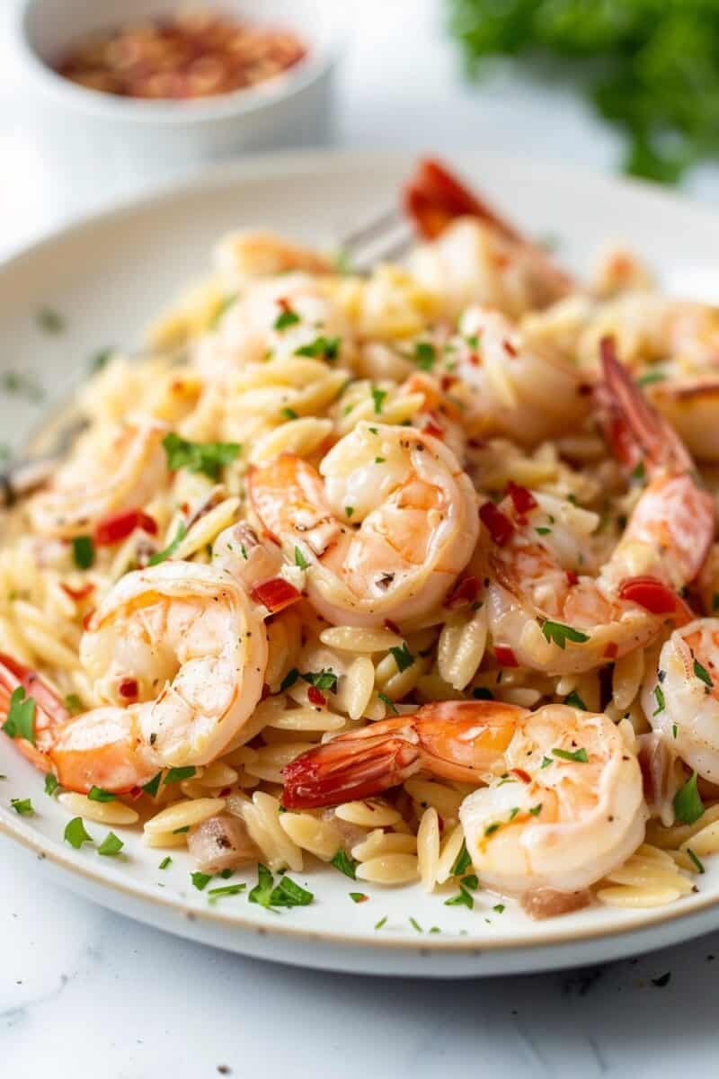 A side view photo capturing garlic butter shrimp served over orzo, highlighting the golden brown shrimp glistening with garlic butter atop a bed of fluffy orzo, garnished with fresh herbs.