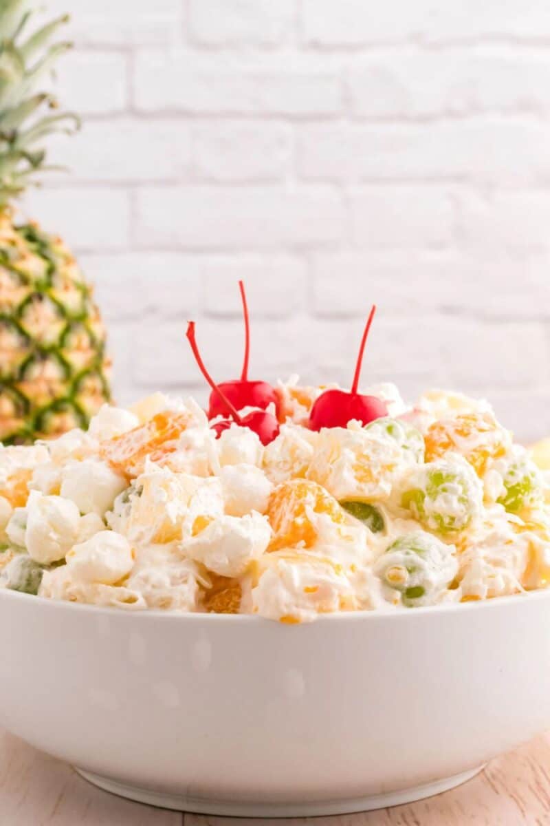 A bowl of Hawaiian Ambrosia Salad, filled with tropical fruits, marshmallows, and coconut flakes, garnished with maraschino cherries.