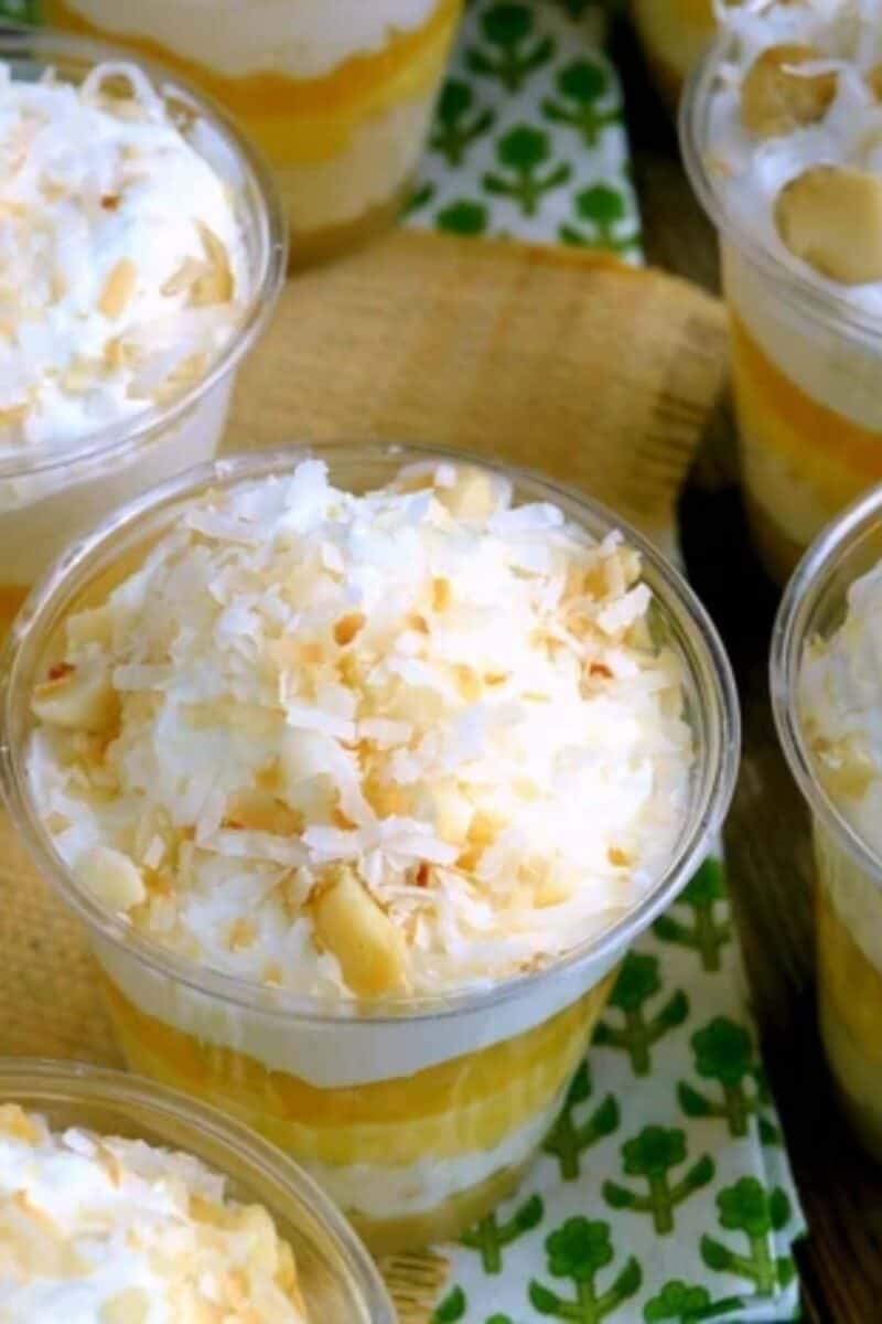 Clear cups layered with yellow pudding and whipped cream, topped with toasted coconut flakes, offering a glimpse of a light and tropical-flavored dessert.