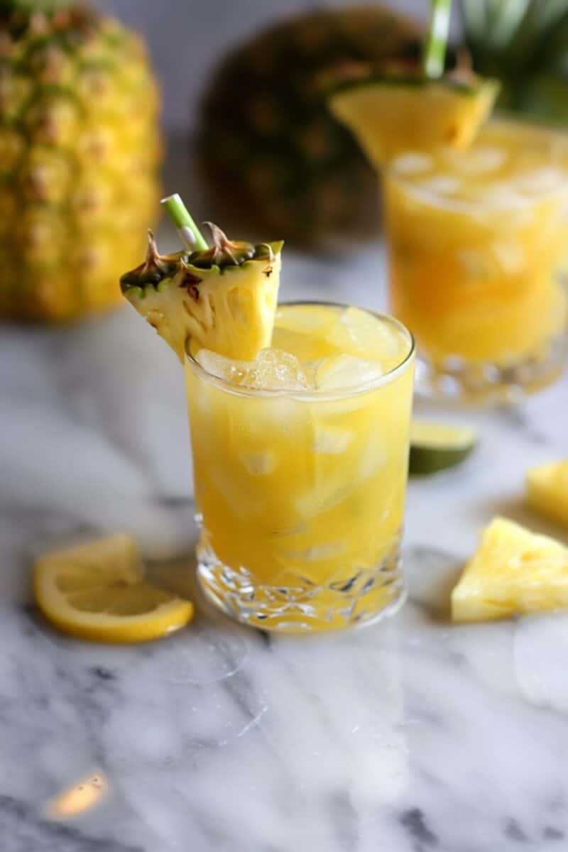 A refreshing glass of vibrant yellow pineapple lemonade, beautifully garnished with a fresh pineapple slice, sits on a pristine white countertop, embodying the essence of summer refreshment.
