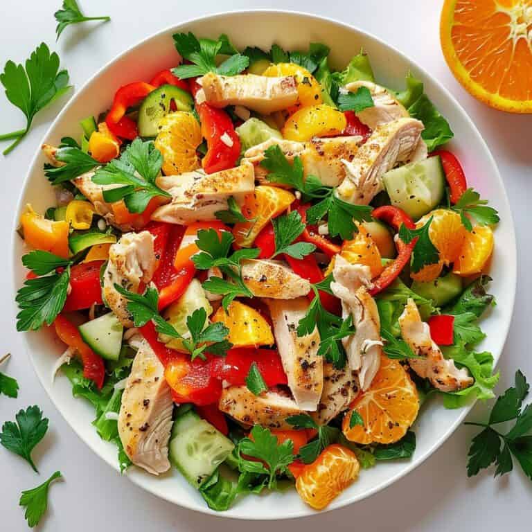 A vibrant chicken citrus salad, featuring grilled chicken strips atop a mix of sliced bell peppers, cucumber, and fresh orange segments, garnished with parsley, perfect for a refreshing spring dinner.