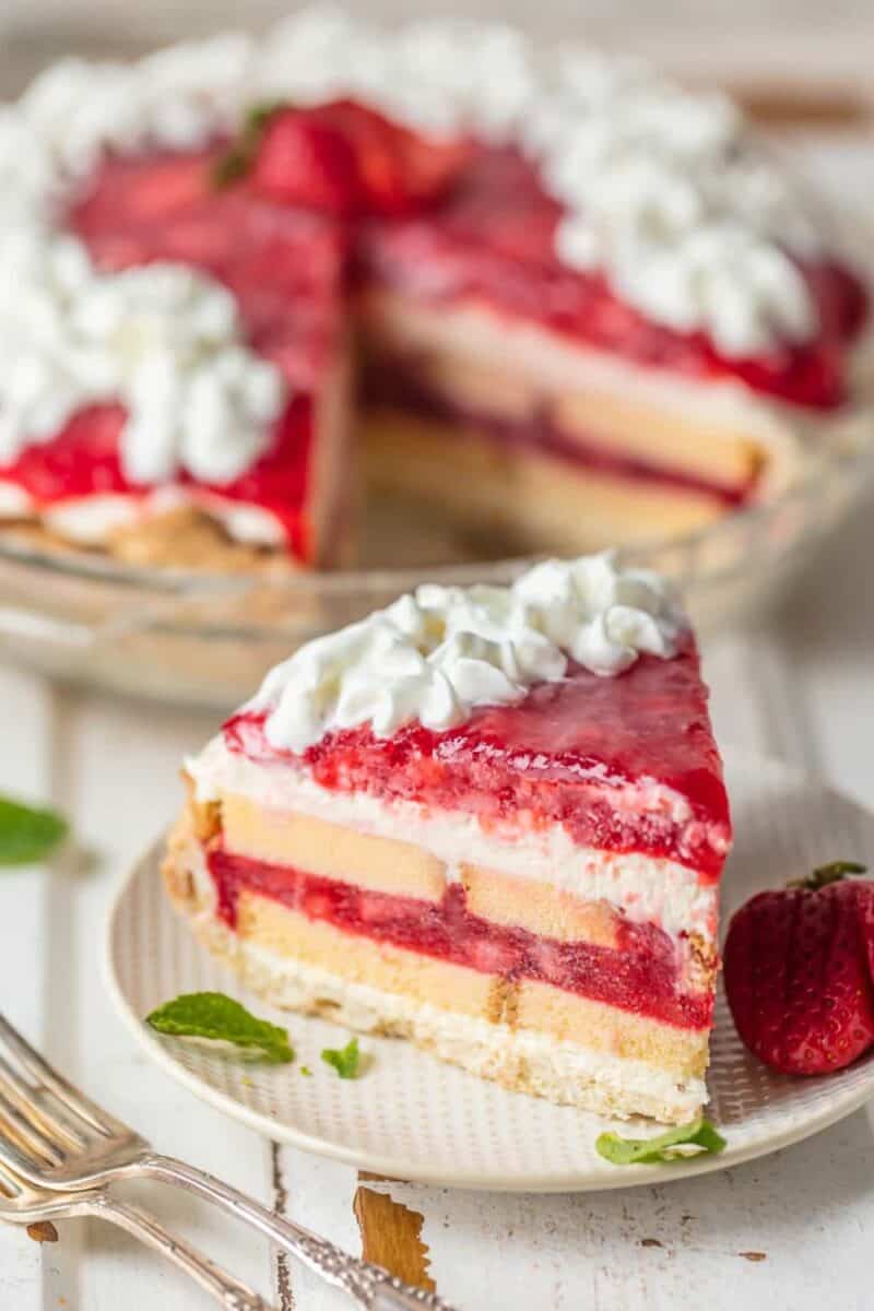 A layered strawberry shortcake pie with vibrant red strawberry filling between layers of cake, topped with whipped cream.
