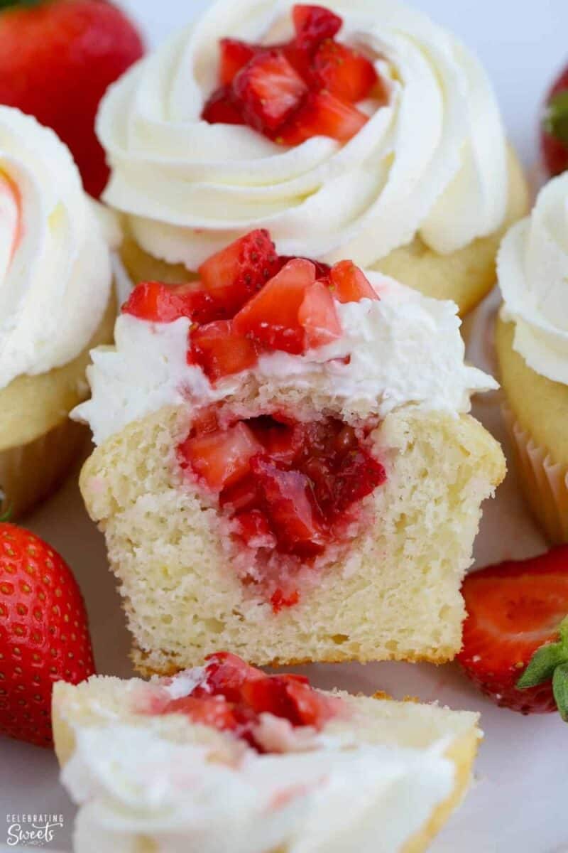 A cupcake cut in half to reveal a creamy strawberry filling, topped with a swirl of whipped cream and a fresh strawberry.