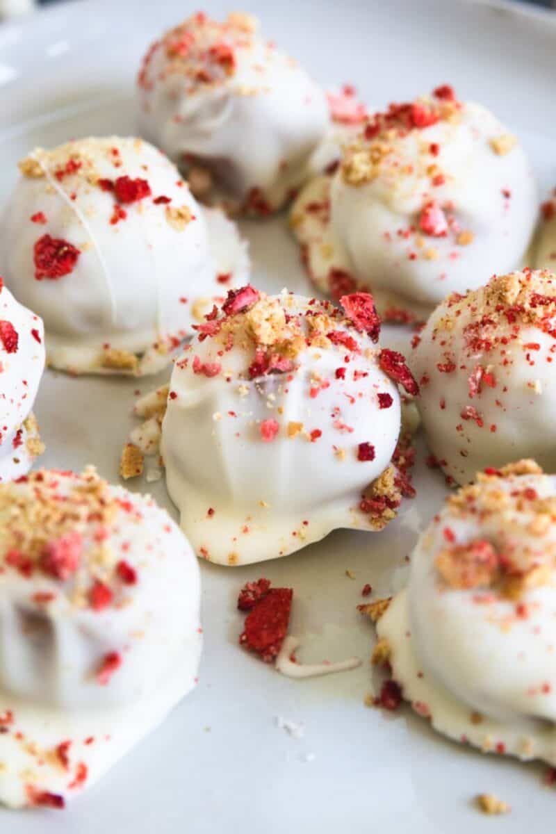 White chocolate-covered strawberry shortcake bites sprinkled with red strawberry dust on a white plate.