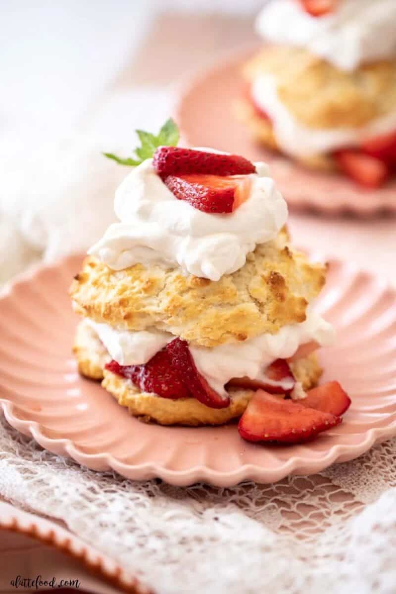 A single serving of strawberry shortcake on a pink plate, featuring a scone-like biscuit, whipped cream, and sliced strawberries.