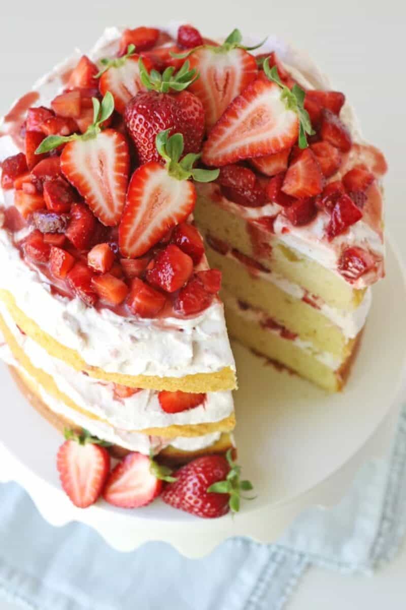 An elegant strawberry shortcake with fresh strawberries and whipped cream between layers of fluffy cake, served on a white plate.