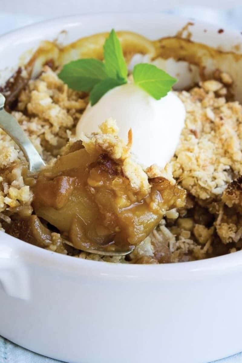 A serving of feijoa crumble in a white bowl, topped with a scoop of vanilla ice cream, garnished with a mint leaf, highlighting the gooey fruit filling.