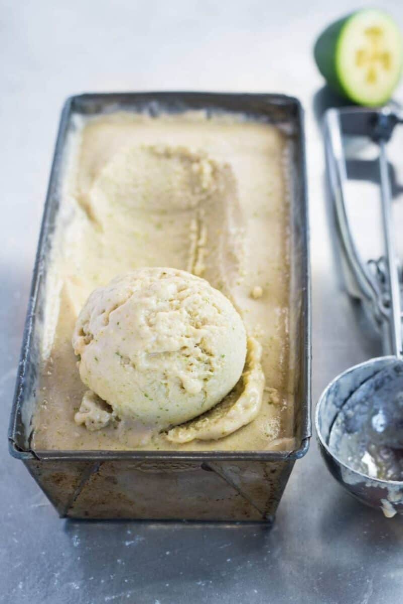 Homemade feijoa ice cream in a metal loaf pan, with a scoop taken out, displaying a pale green color indicative of the fruit's inclusion.
