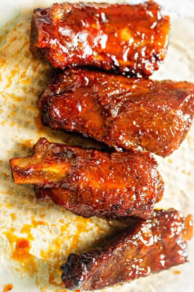 Sticky pork ribs glazed in a rich, feijoa sauce, artfully plated with sauce drizzles on parchment paper, showcasing a shiny, caramelized exterior.