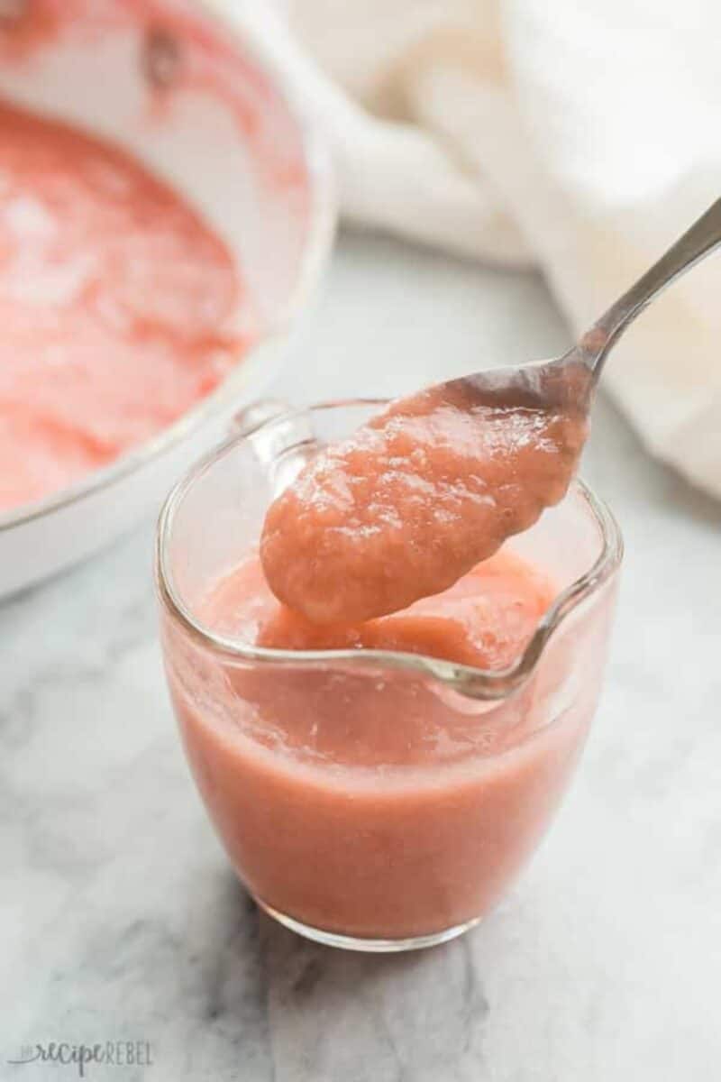 A glass of rhubarb sauce with a spoon scooping out some of the thick, pale pink mixture, suggesting a velvety texture.
