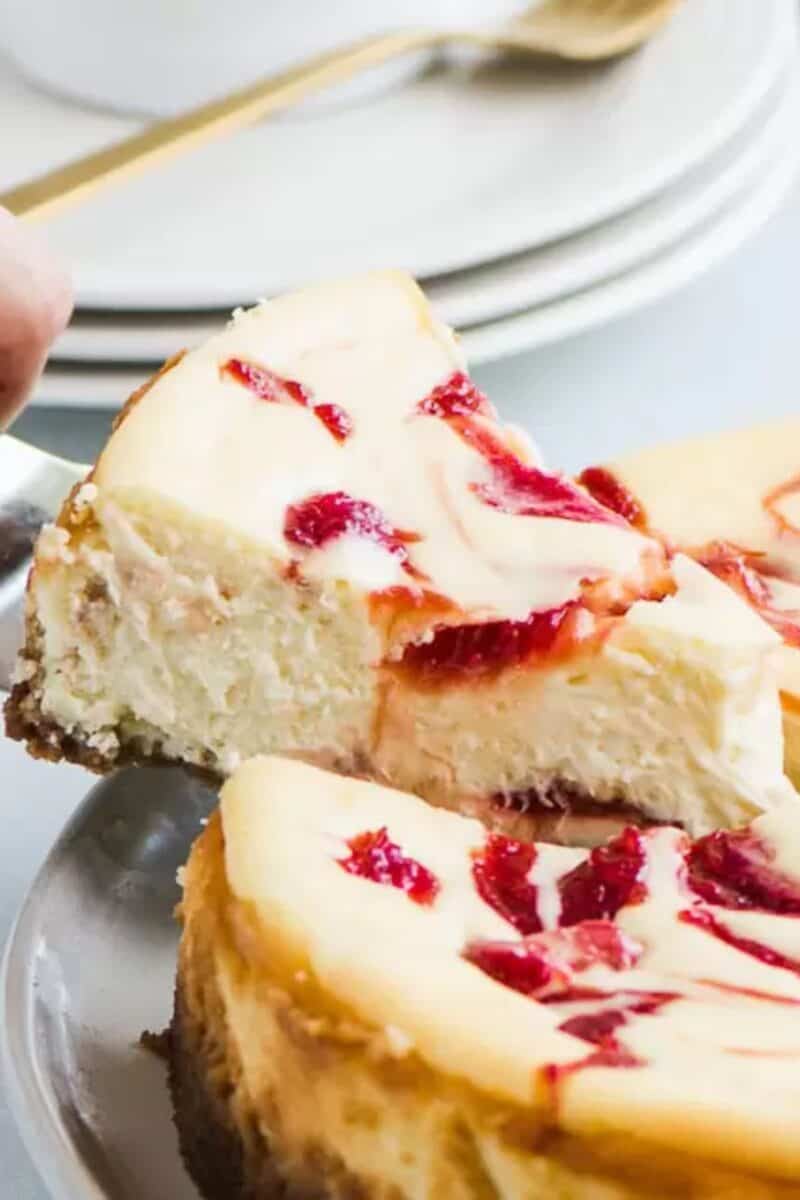 Creamy rhubarb cheesecake with a vibrant red rhubarb swirl topping on a white plate with a silver fork.